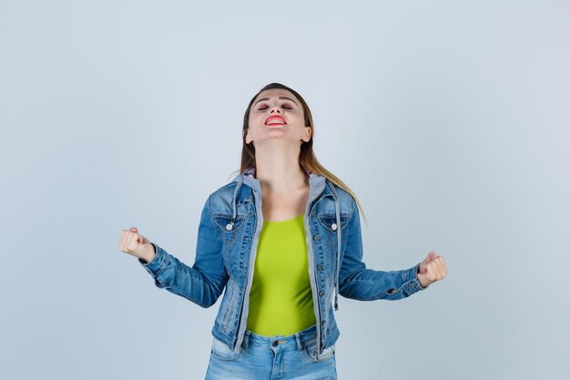 Jovem senhora em roupa de jeans, mostrando o gesto do vencedor e parecendo com sorte, vista frontal.