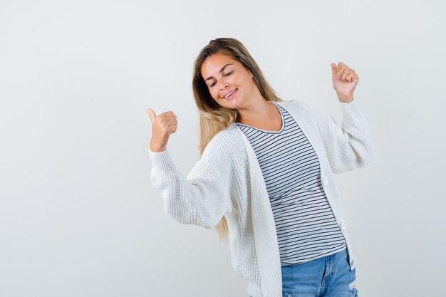 Jovem senhora em t-shirt, jaqueta mostrando dois polegares para cima e parecendo feliz, vista frontal.