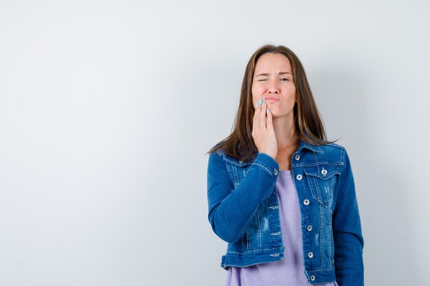 Jovem senhora em t-shirt, jaqueta, sofrendo de dor de dente e parecendo incomodada, vista frontal.