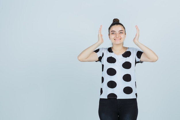 Jovem senhora em t-shirt, jeans, mostrando sinal de tamanho e parecendo feliz, vista frontal.