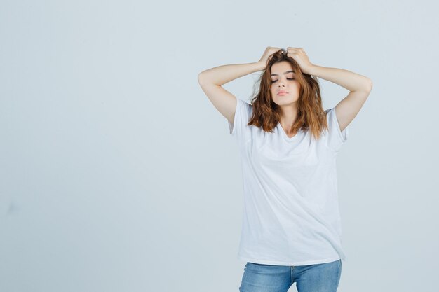 Jovem senhora em t-shirt, jeans, segurando as mãos na cabeça e parecendo sombrio, vista frontal.