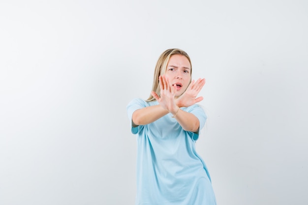 Jovem senhora em t-shirt, mostrando o gesto de recusa e olhando com medo, vista frontal.