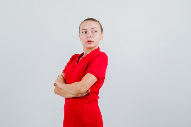 Jovem senhora olhando para longe com os braços cruzados em uma camiseta vermelha e parecendo confiante