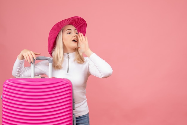 Jovem senhora parada atrás de uma mala rosa ligando para alguém