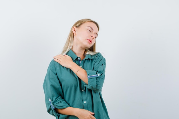 Jovem senhora que sofre de dor no ombro em uma camisa verde e parece desconfortável.
