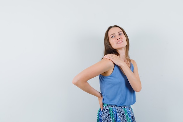 Jovem senhora que sofre de dor no ombro na camiseta, saia e parece cansada. vista frontal.