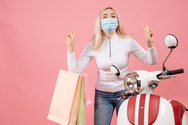 Jovem senhora segurando sacolas de compras fazendo sinal de vitória perto de motocicleta