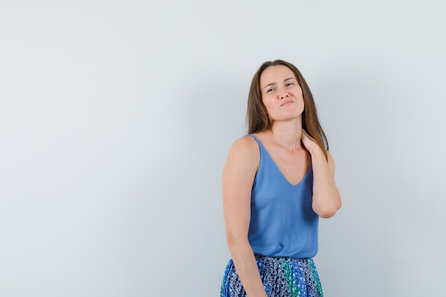 Jovem senhora sofrendo de dor no pescoço na camiseta, saia e parecendo irritada, vista frontal.