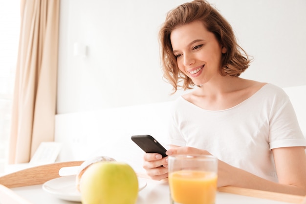 Jovem senhora sorridente, sentado dentro de casa, conversando por telefone.