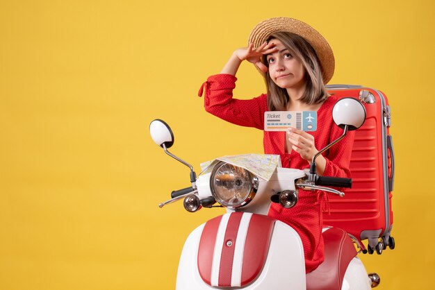 Jovem senhora vestida de vermelho segurando bilhete e observando em ciclomotor