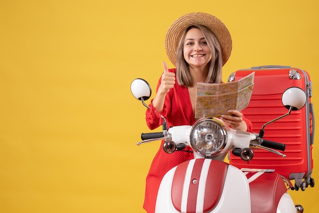 Jovem senhora vestida de vermelho segurando um mapa e mostrando o polegar para cima perto de uma motocicleta