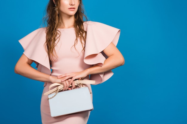 Jovem sensual elegante em um vestido rosa de luxo, tendência da moda de verão, estilo chique, fundo azul studio, segurando uma bolsa da moda