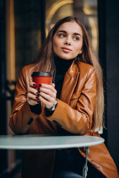 Jovem sentada do lado de fora do café tomando café