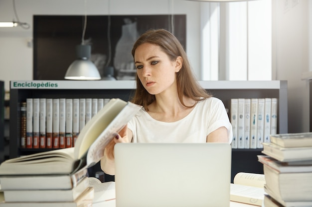 Jovem sentada na biblioteca com um laptop