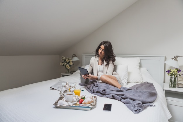 Foto grátis jovem sentada na cama e usando seu tablet