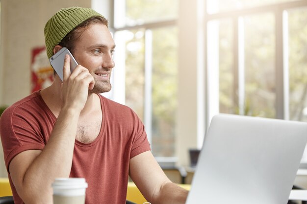 Jovem sentado em um café com laptop e telefone