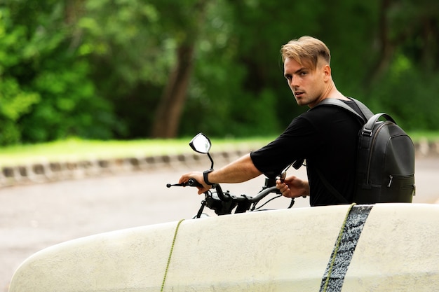 Jovem sentado em uma motocicleta com uma prancha de surf