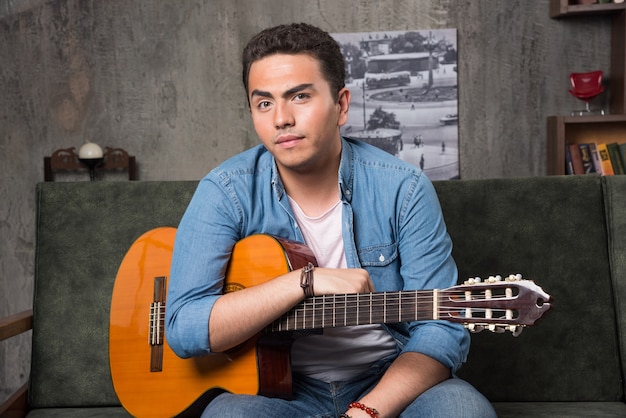 Jovem sentado no sofá com uma bela guitarra. Foto de alta qualidade