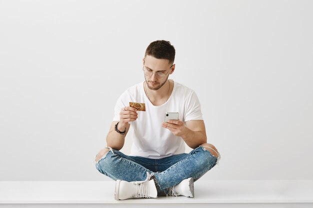 Jovem sério de óculos, posando com seu telefone e cartão