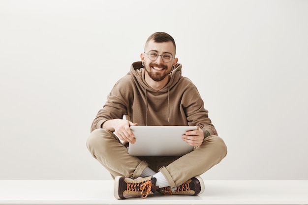 Jovem simpático sentado com um laptop e sorrindo