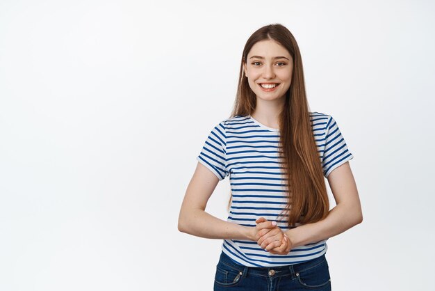 Jovem sorridente ajudando de mãos dadas e olhando amigável para a câmera posando contra fundo branco