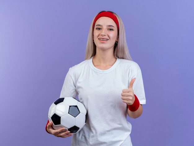 Jovem sorridente caucasiana desportiva com aparelho e faixa na cabeça