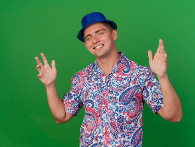 Foto grátis jovem sorridente com chapéu azul e as mãos isoladas no fundo verde.