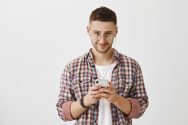 Foto grátis jovem sorridente de óculos posando com seu telefone e fones de ouvido