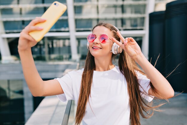 Jovem sorridente e dançando fazendo uma selfie com seu smartphone e ouvindo música em fones de ouvido