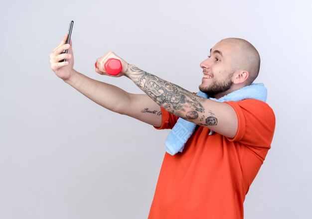 Jovem sorridente e desportivo segurando halteres e tirar uma selfie isolada no branco
