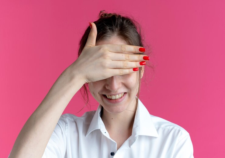 Foto grátis jovem sorridente loira russa esconde os olhos com a mão isolada no espaço rosa com espaço de cópia