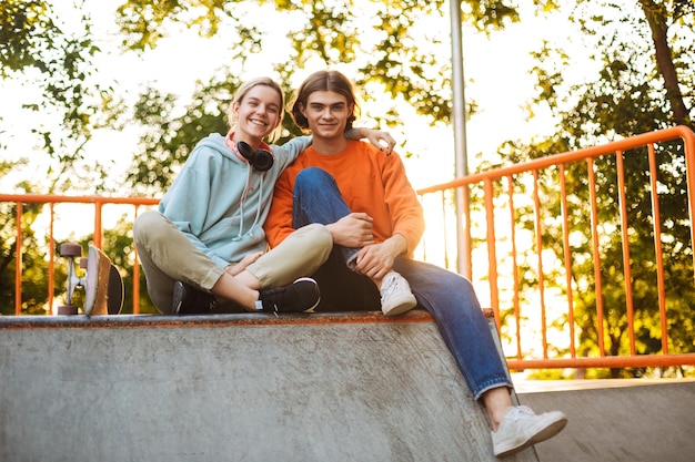 Jovem sorridente menino e menina olhando alegremente para a câmera enquanto passam tempo juntos no skatepark