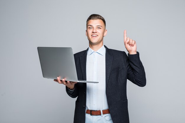 Jovem sorridente posando com o telefone laptop vestido com uma jaqueta escura em estúdio isolado na parede cinza