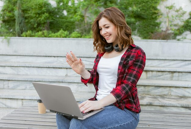 Jovem sorridente se comunica em uma videochamada ou cumprimenta seus assinantes ao ar livre. tema de estudante ou blogueiro Foto Premium