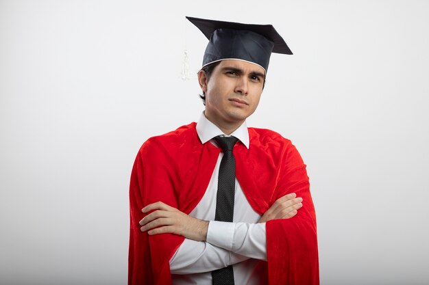 Jovem super-herói confiante olhando para a câmera usando gravata e chapéu de pós-graduação cruzando as mãos