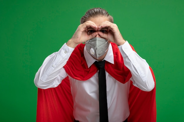 Foto grátis jovem super-herói usando máscara médica e gravata, mostrando gesto de olhar isolado sobre fundo verde