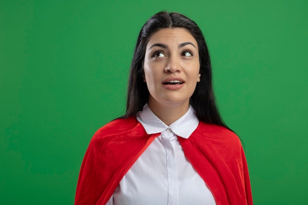 Foto grátis jovem super-heroína caucasiana impressionada de pé, sem nenhuma placa, olhando para cima isolada no fundo verde com espaço de cópia