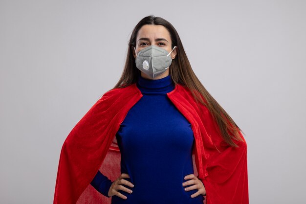 Jovem super-heroína confiante usando máscara médica, colocando as mãos no quadril, isolado no fundo branco