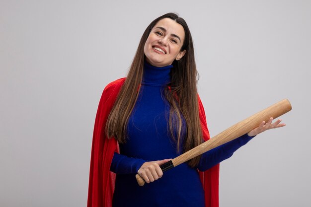 Jovem super-heroína sorridente segurando um taco de beisebol isolado no branco