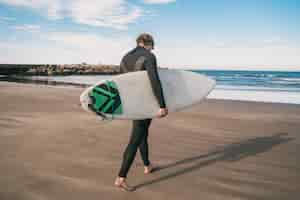 Foto grátis jovem surfista em pé no oceano com sua prancha de surf em um terno preto de surf. esporte e conceito de esporte aquático.