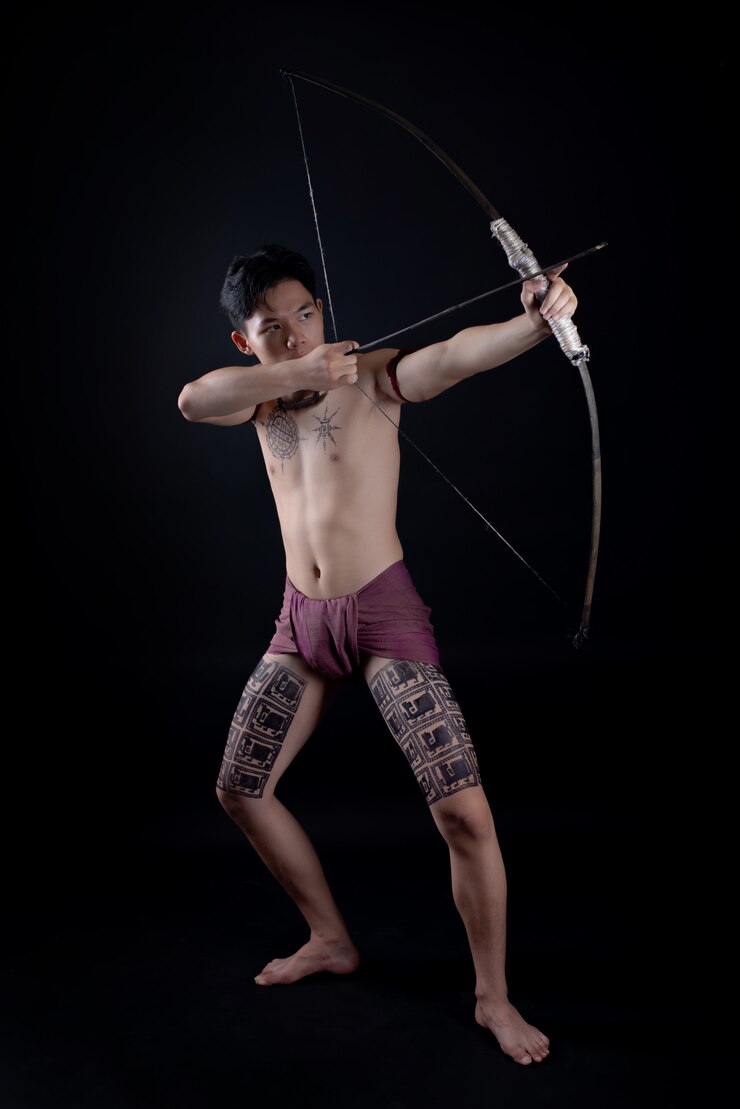 Foto grátis jovem tailândia guerreiro masculino posando em uma posição de luta com um arco