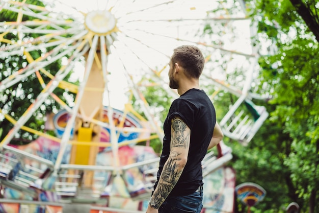 Jovem tatuado em um parque de diversões no fundo de um goleiro