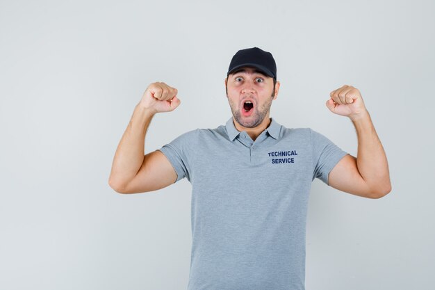 Jovem técnico de uniforme, mostrando o gesto do vencedor e parecendo feliz.