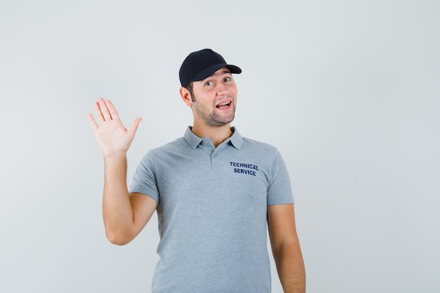 Jovem técnico em uniforme cinza acenando com a mão para saudar e olhar alegre.