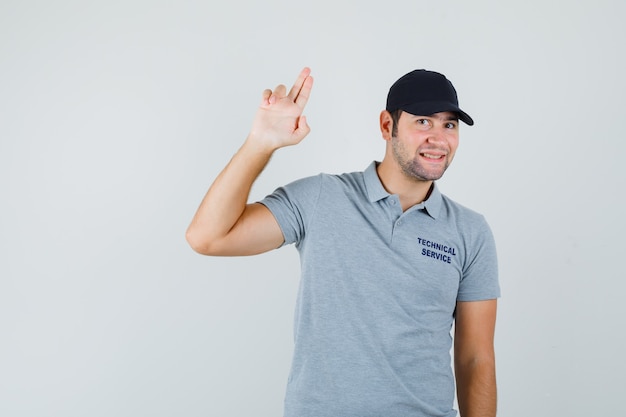 Jovem técnico fazendo sinal de pistola de dedo em uniforme cinza e parecendo alegre.