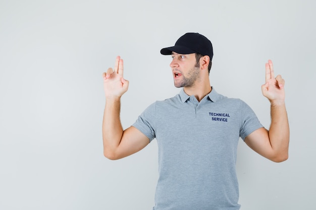 Jovem técnico fazendo sinal de pistola de dedo em uniforme cinza e parecendo confiante.