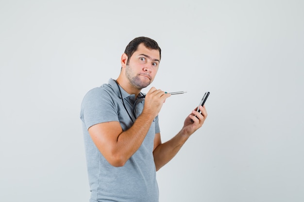 Jovem técnico tentando abrir a parte de trás de seu smartphone usando broca de uniforme cinza e parecendo curioso.