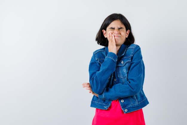 Jovem tendo dor de dente em uma camiseta vermelha e jaqueta jeans e parecendo exausta. vista frontal.