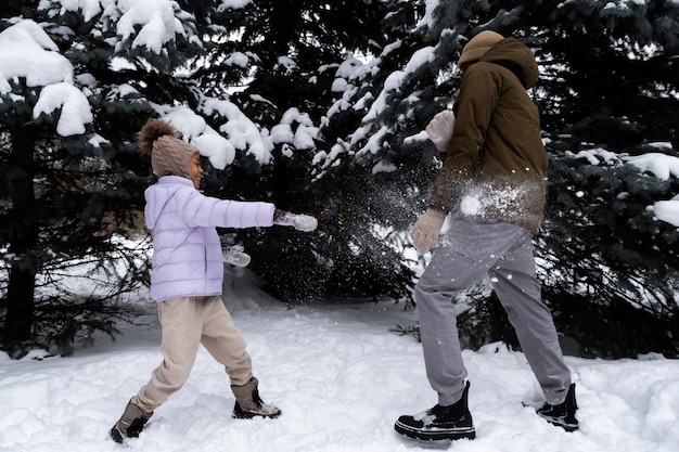 Foto grátis jovem tendo uma luta de neve com o pai em um dia de inverno
