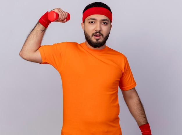 Jovem tenso e esportivo usando bandana e pulseira, fazendo exercícios com halteres isolados no fundo branco